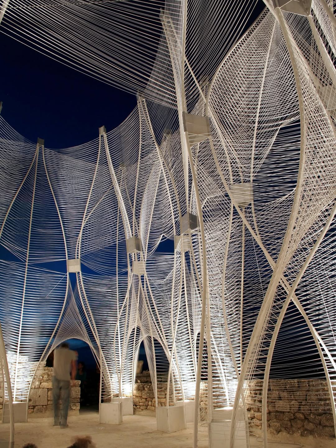 🌬️Designed by @narchitects_pllc and built with SCAD students in Lacoste, France, Windshape reimagines how architecture can breathe with its environment. The project transformed two eight-meter-high pavilions into living instruments shaped by the Provençale wind. A lattice of bent plastic pipes and more than fifty kilometers of woven polypropylene string created shifting enclosures that rippled, hissed, and continually changed form throughout the summer of 2006.

Rather than resisting the elements, Windshape embraced them, turning wind into structure, movement, and atmosphere. Positioned between the limestone village of Lacoste and the soft agricultural landscape of Provence, the installation became the town’s main gathering space, hosting concerts, exhibitions, and nightly illuminations against the looming silhouette of the Marquis de Sade’s castle.

👩‍🎓Join @thepaacademy’s workshops to learn the most advanced tools in architecture and fashion design from pioneering architects and designers!

📸 @narchitects_pllc

#parametricarchitecture #narchitects #scad #installationart #dynamicarchitecture #lacosse #windstructure #experimentalarchitecture