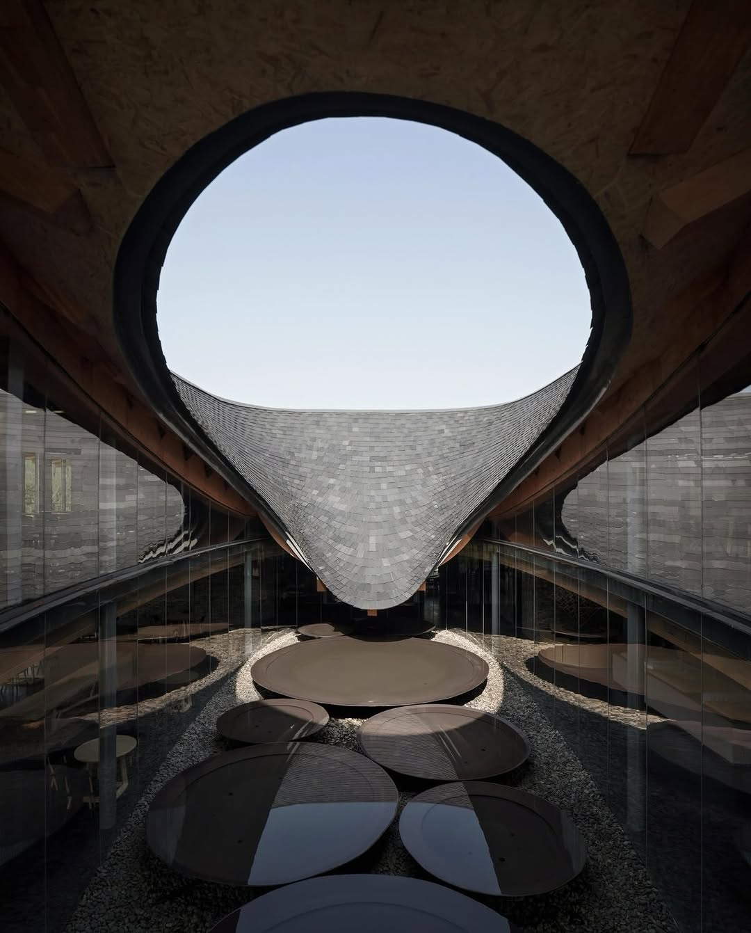 📌Inkstone House / Archi-Union Architects

The Inkstone House, designed by @archi_union, sits at the heart of the OCT Linpan Cultural Center in Anren, China. The project features a distinctive U-shaped tiled roof that folds inward to create a central courtyard. The flowing roof form echoes the soft topography of Sichuan’s landscape, while simultaneously defining a contemplative spatial experience.

Timber beams, mirrored surfaces, and fluid geometries define the interior language, creating a serene contrast between craftsmanship and computational precision. The building draws inspiration from traditional inkstones, tools used in Chinese calligraphy, and reinterprets them through contemporary digital design methodologies.

📸 Shengliang Su, Tianzhou Yang

#InkstoneHouse #ContemporaryArchitecture #ChineseArchitecture