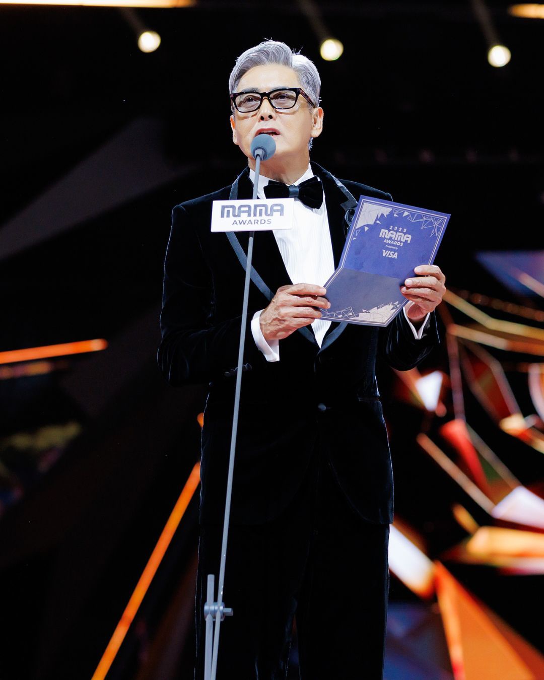 香港大埔宏福苑日前發生嚴重火災，MAMA 2025 主辦方迅速應變，將頒獎禮主題調整為「Support Hong Kong」，透過一系列低調而莊重的安排向災民致意與悼念。包括取消紅毯、減少燈光特效、降低音量，所有頒獎嘉賓佩戴黑絲帶，演出藝人也換上黑白色系服裝。主辦方同時宣布捐款 2000 萬港幣，多家韓國娛樂公司及藝人亦紛紛響應捐款，展現跨地域的關懷與支持。

第二晚典禮中，香港影星周潤發身穿黑色西裝壓軸登場，在頒發「年度藝人」前，他帶領全場起立，為火災遇難者與傷者默哀一分鐘。此舉凝聚了在場觀眾與藝人的心意，彰顯音樂與人文精神的力量，也讓本屆 MAMA 在追悼與團結中，留下了深刻而溫暖的印記。

Following the devastating fire at Hung Fook Court in Tai Po, Hong Kong, the organizers of MAMA 2025 responded swiftly, changing the theme of the awards ceremony to “Support Hong Kong.” Through a series of understated yet solemn arrangements, they paid tribute to and mourned the victims. These included canceling the red carpet, reducing lighting effects, lowering volume, requiring all award presenters to wear black ribbons, and having performing artists change into black and white attire. The organizers also announced a donation of HK$20 million, with several Korean entertainment companies and artists responding with donations, demonstrating cross-regional care and support.

On the second night of the ceremony, Hong Kong film star Chow Yun-fat, dressed in a black suit, made a grand entrance as the finale. Before presenting the “Artist of the Year” award, he led the audience in a minute’s silence for the fire victims and injured. This gesture united the hearts of the audience and artists present, highlighting the power of music and humanitarianism, and leaving a profound and heartwarming mark on this year’s MAMA through remembrance and solidarity.

Credit @mnet_mama 

👉🏻follow us @ellehongkong #mama #周潤發 #SupportHongKong